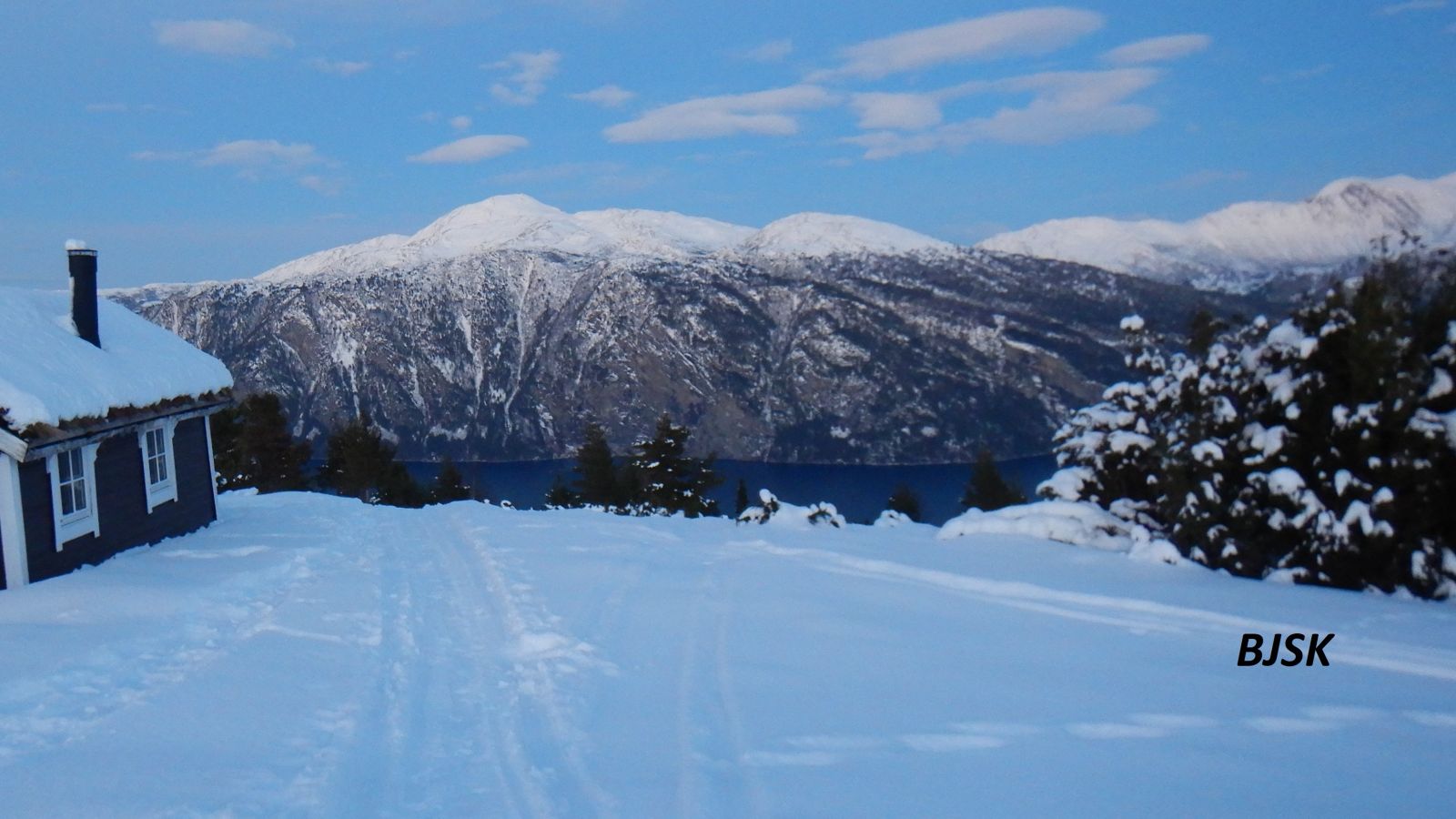 Seterbu i snødekt åpent landskap med utsikt til fjord og fjell.