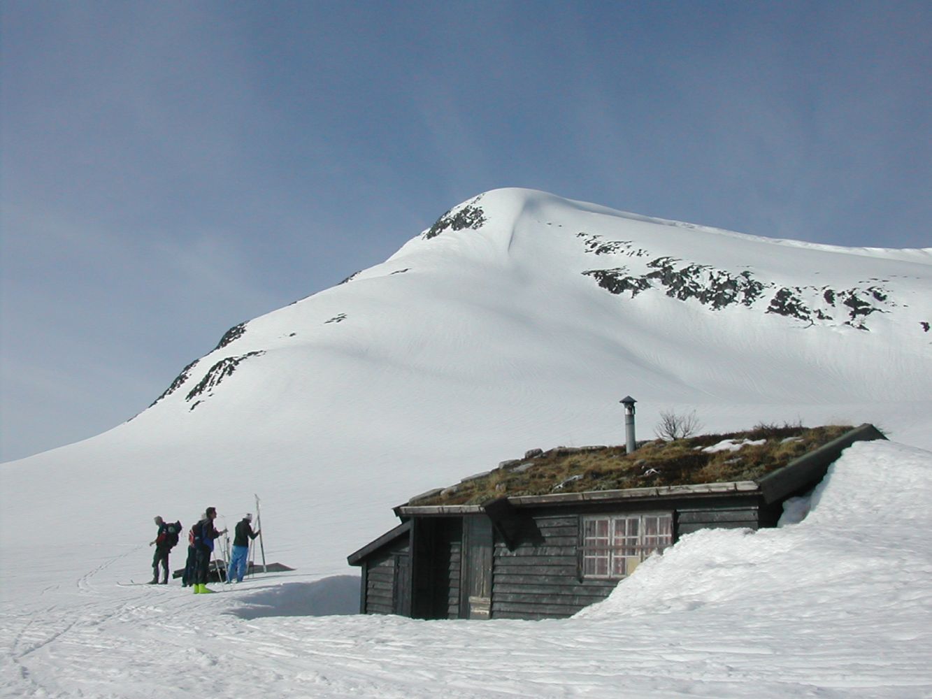 Fire skiløpere har tatt av seg skiene og har pause utenfor hytte.
